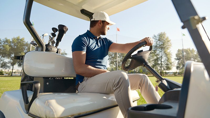 golfer,riding,golf,cart,on,green,lawn,of,golf,field