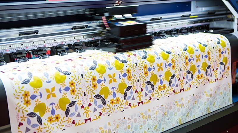 a large format printer printing a colorful design onto a roll of transfer paper