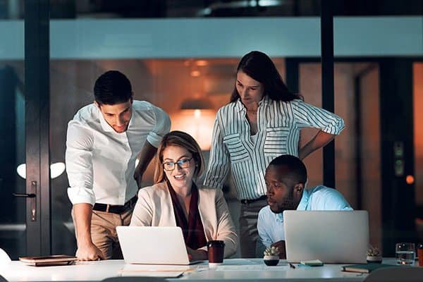 collaboration, team diversity and office at night for deadline, strategy and explanation with laptop. female leader, group and workshop for learning, growth and development in workplace in evening